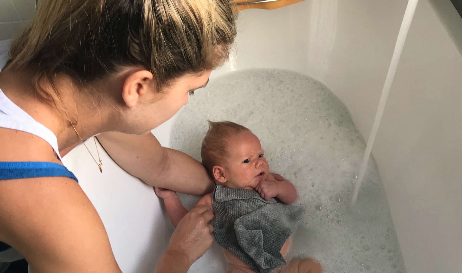 A newborn being gently bathed in a bubble bath, supported by a parent