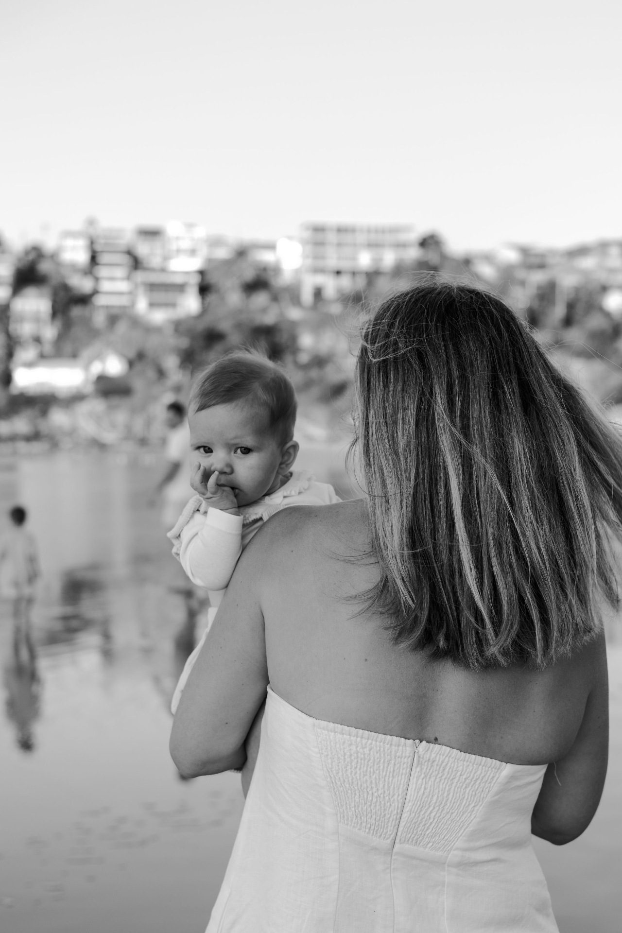 A mother carrying her baby over her shoulder looking out toward the beach