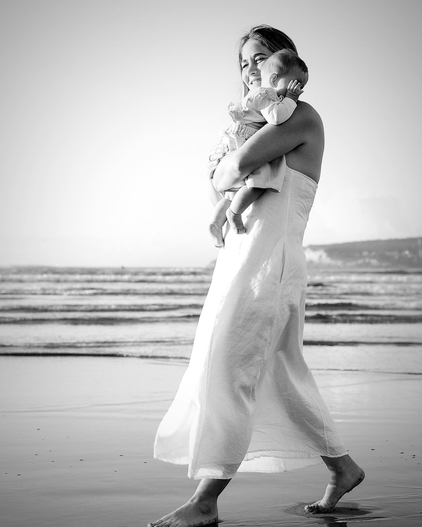 Jane walking barefoot along the shoreline holding her baby close